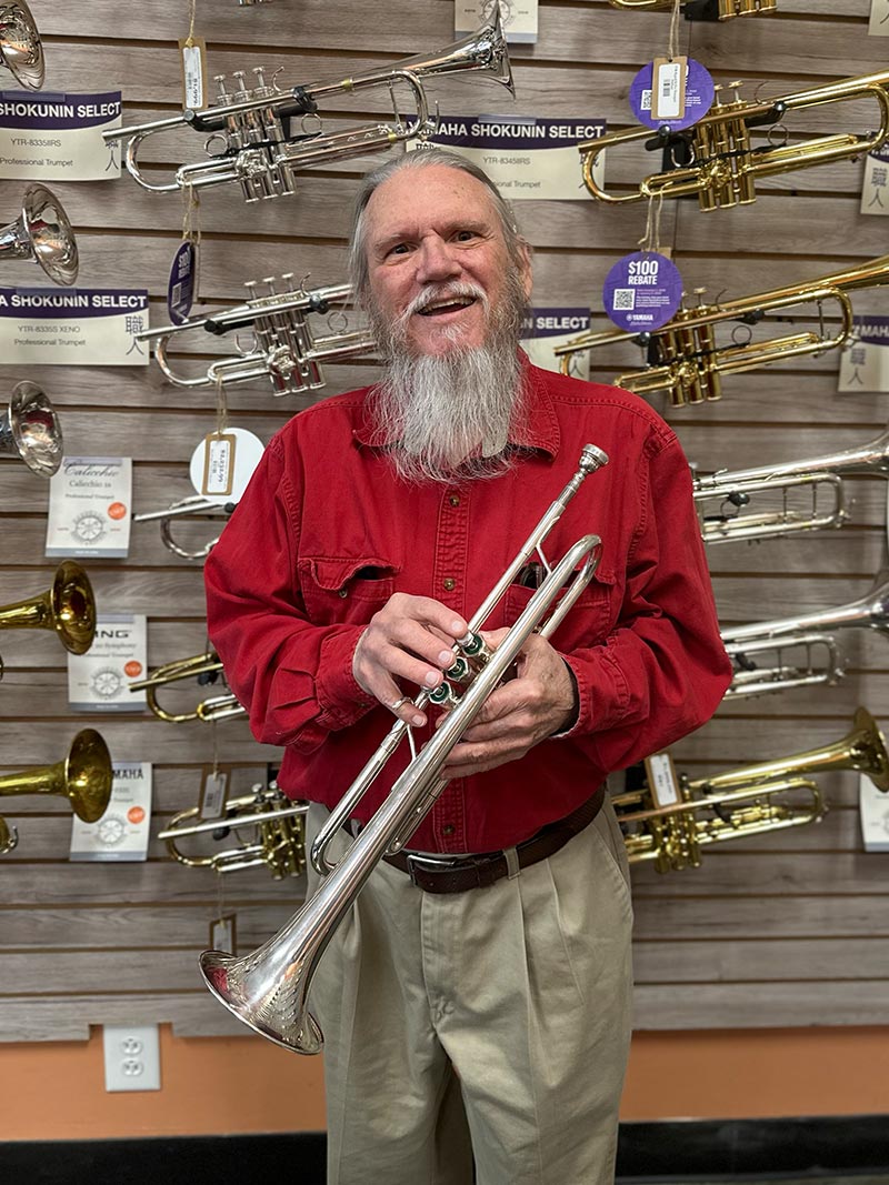 Tom Mcintire standing in front of a wall of trumpets.