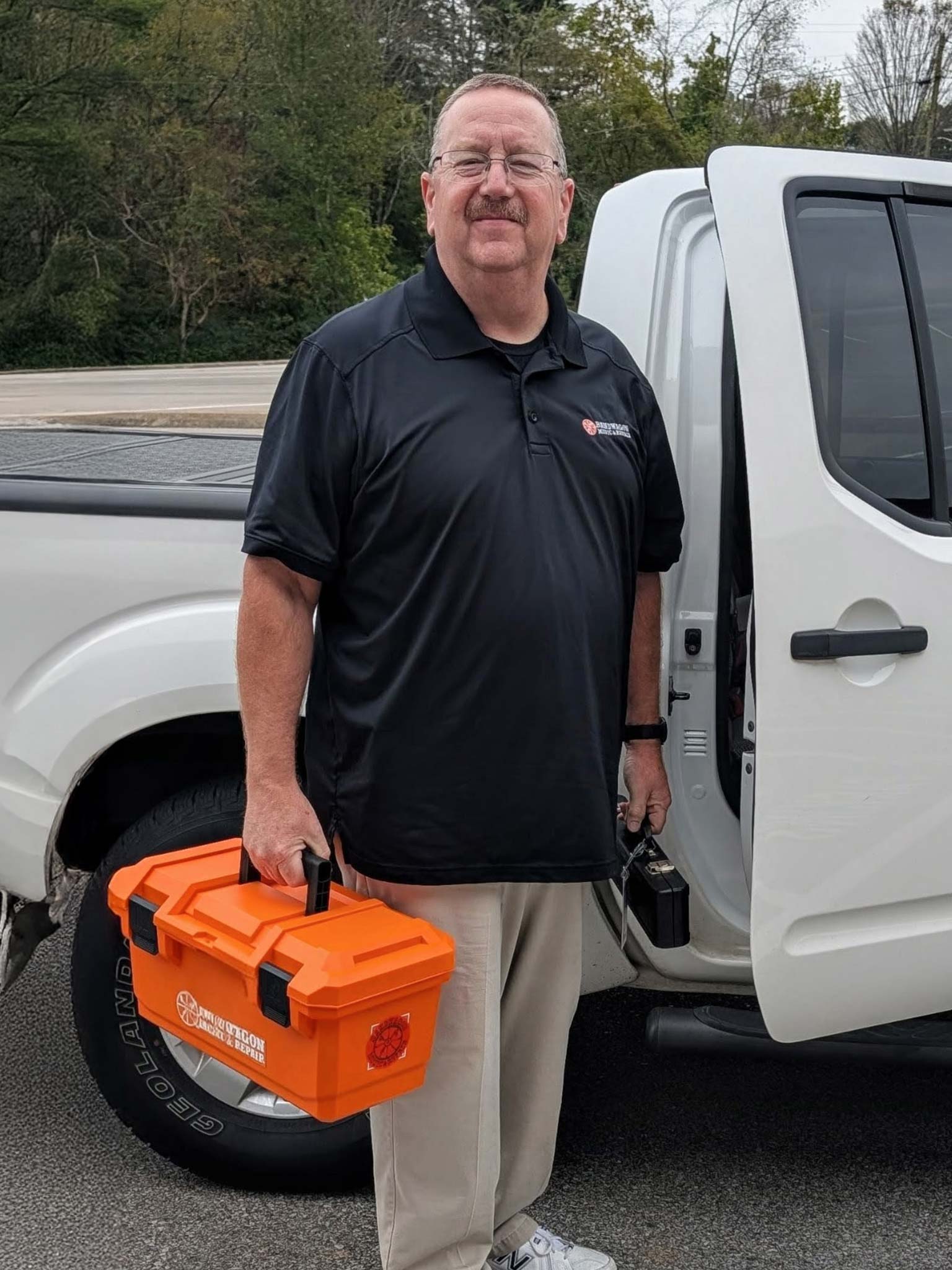 Chuck standing beside a white truck with music repair tools in hand
